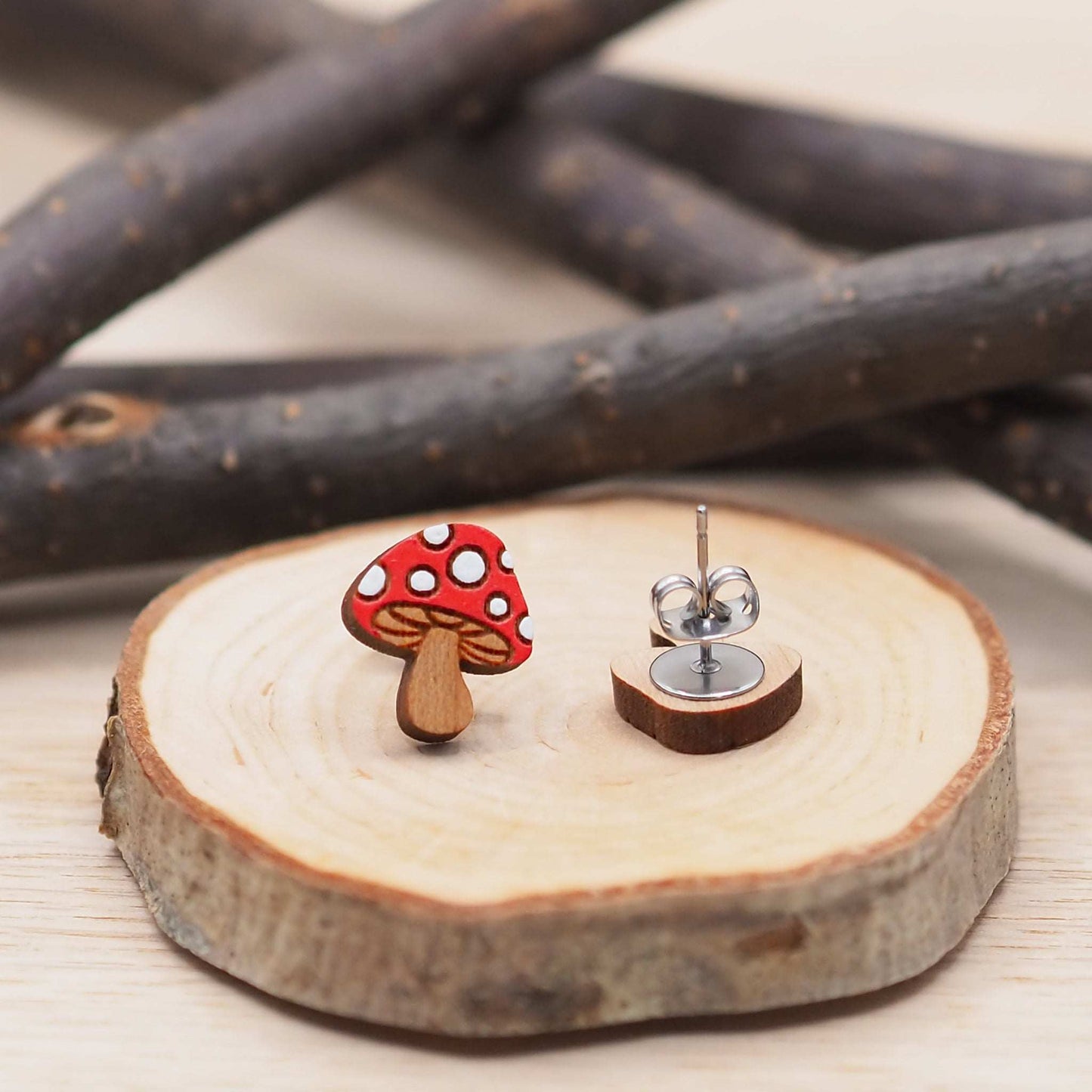 Hand-painted red and white mushroom stud earrings made from solid cherry wood on a natural wood slice.