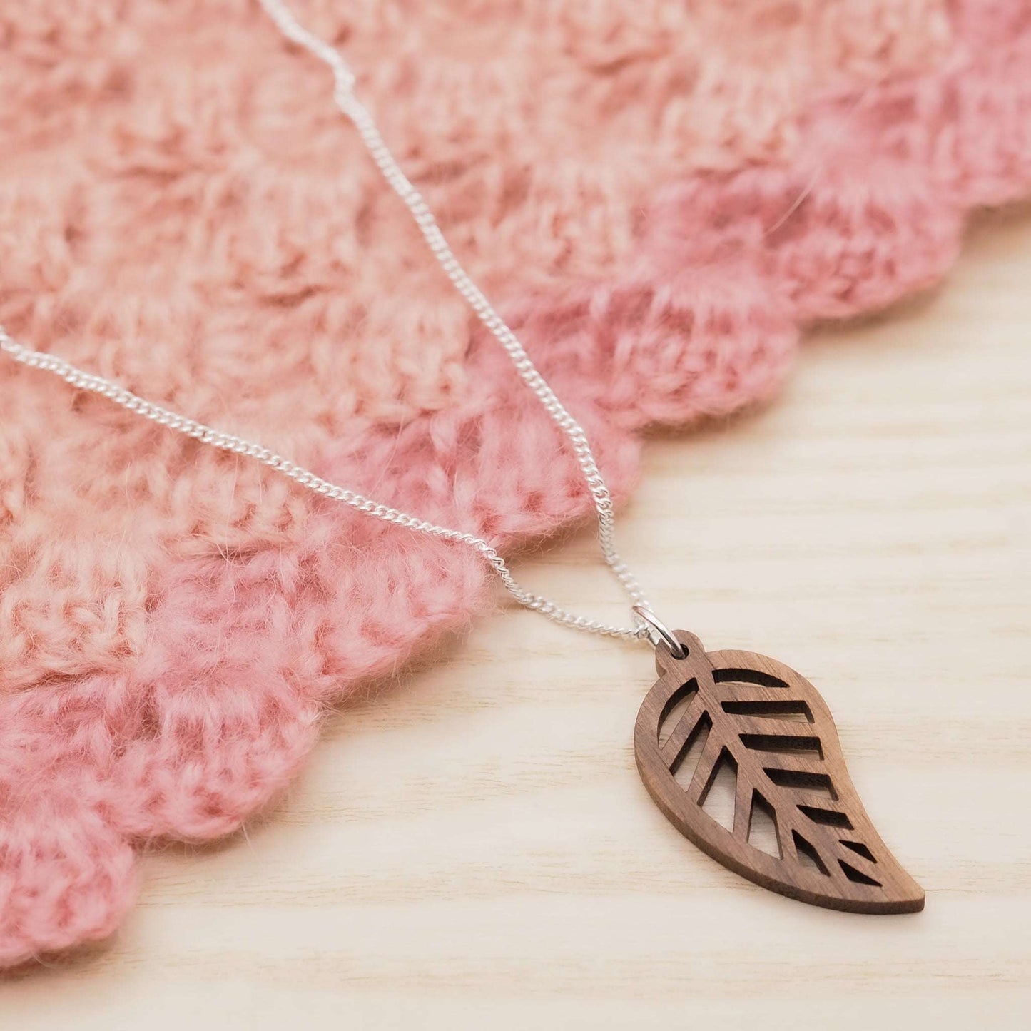 Leaf outline necklace on a pink textured background, featuring a walnut wood pendant on a recycled sterling silver chain.