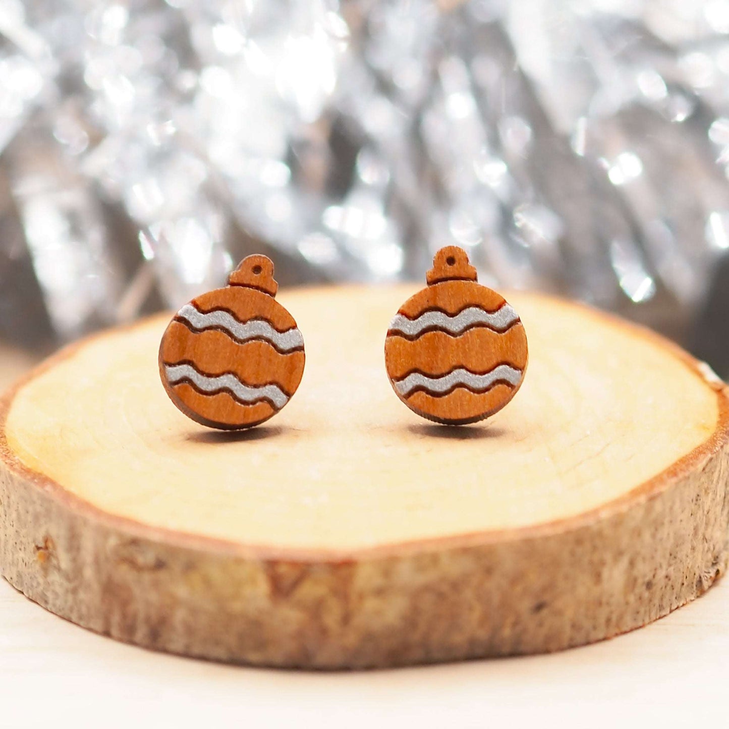 Silver Christmas bauble earrings on wood, featuring hand-painted silver pattern with surgical steel posts.