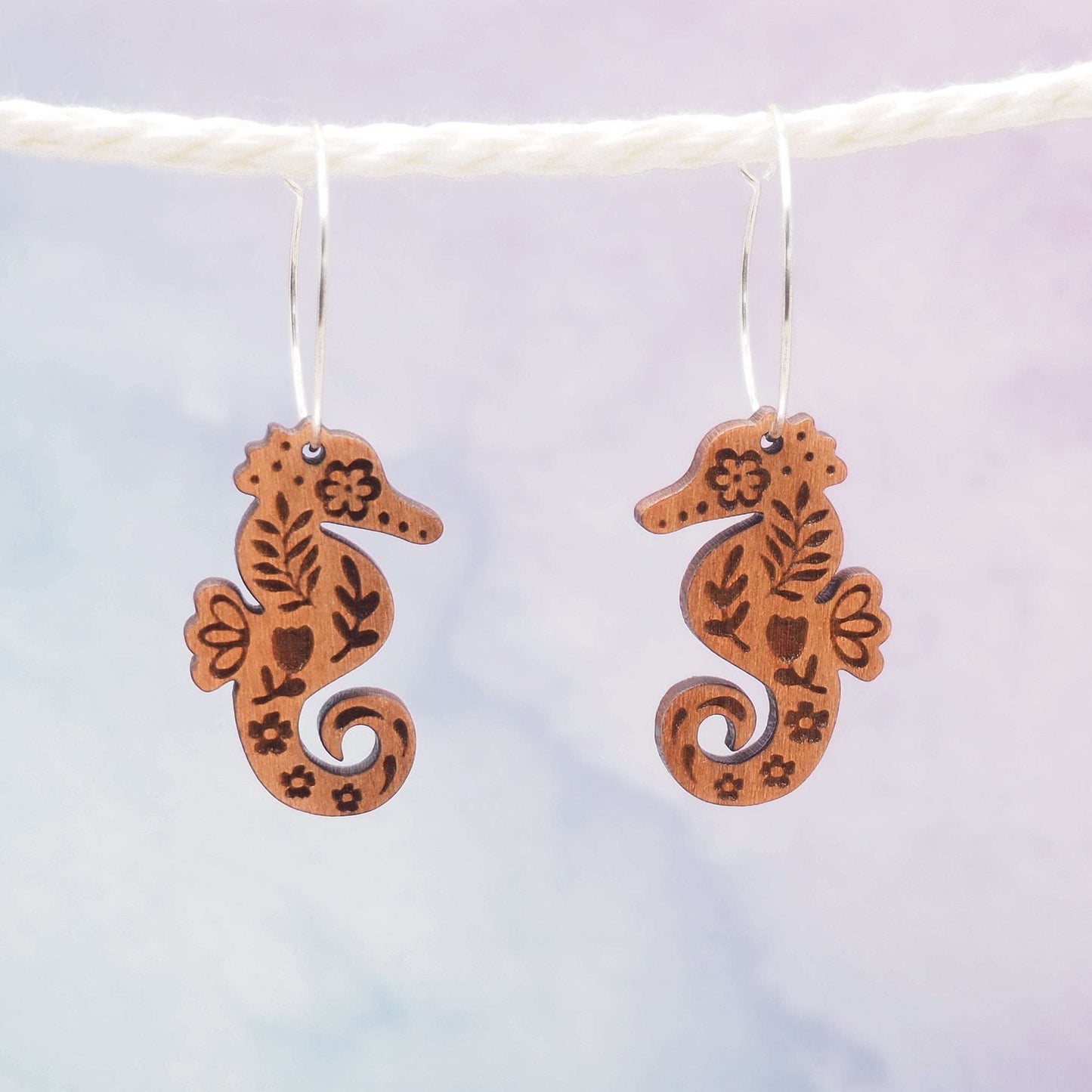 Seahorse engraved hoop earrings made from sustainable cherry wood with sterling silver hoops, featuring a folksy style pattern, and eco-friendly varnish.
