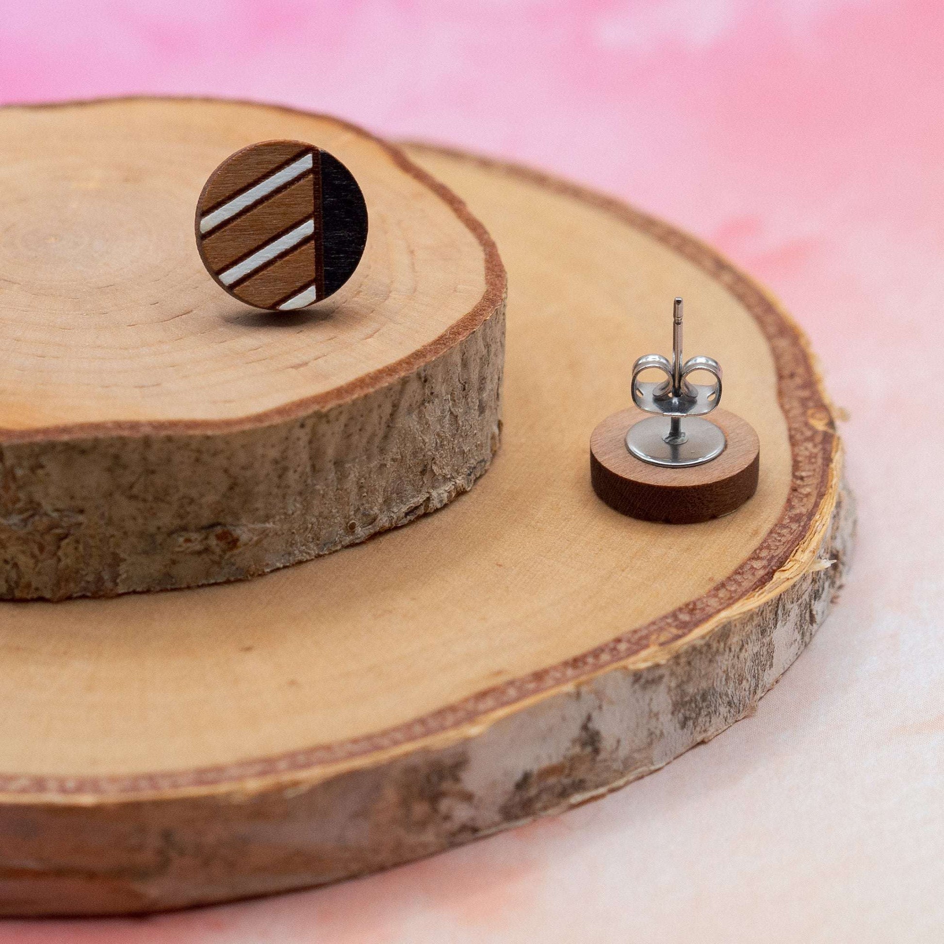 Monochrome geometric painted stud earrings on wooden surface with pink background.