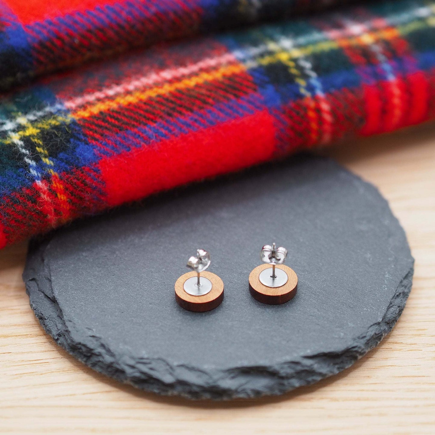 Cherry wood stag head stud earrings with surgical steel posts on slate surface, tartan fabric background.