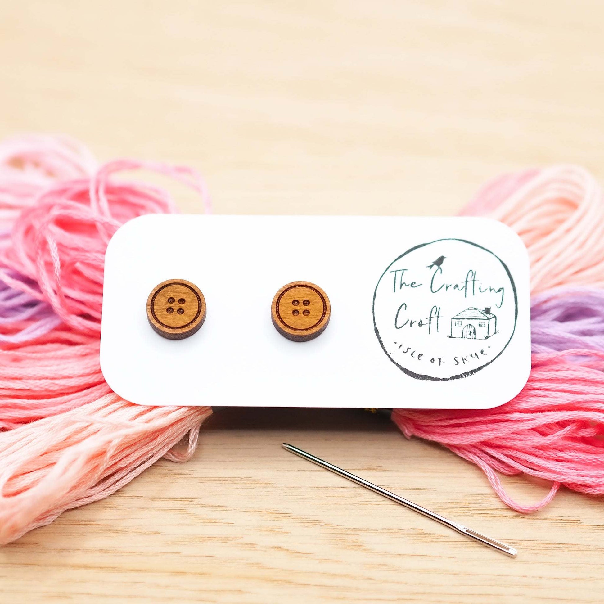 Cherry wood button stud earrings with surgical steel backs, presented on a card with colorful yarn background.