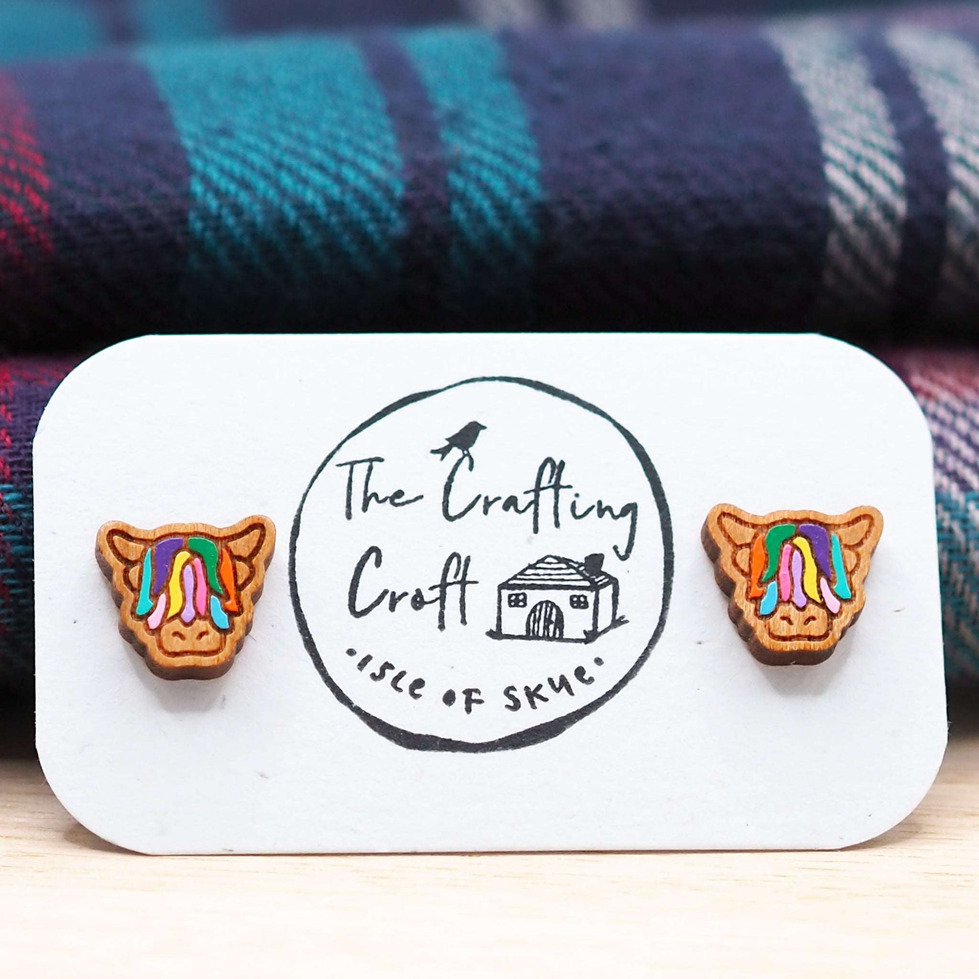 Multi-coloured Highland Cow stud earrings made from cherry wood with surgical steel backs on a presentation card.
