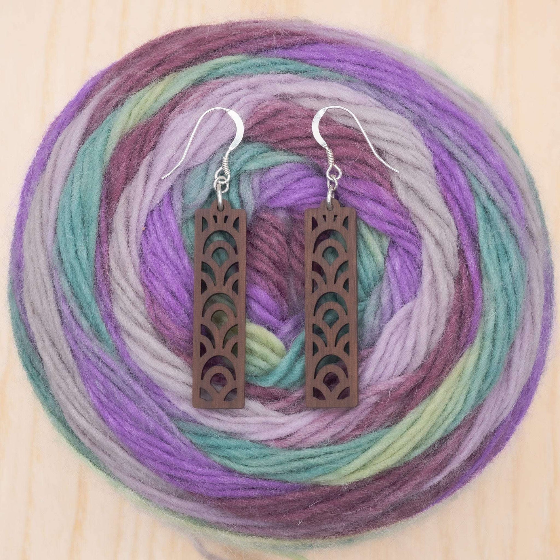 Geometric design drop earrings made from walnut wood with sterling silver hooks, presented on a colorful yarn background.
