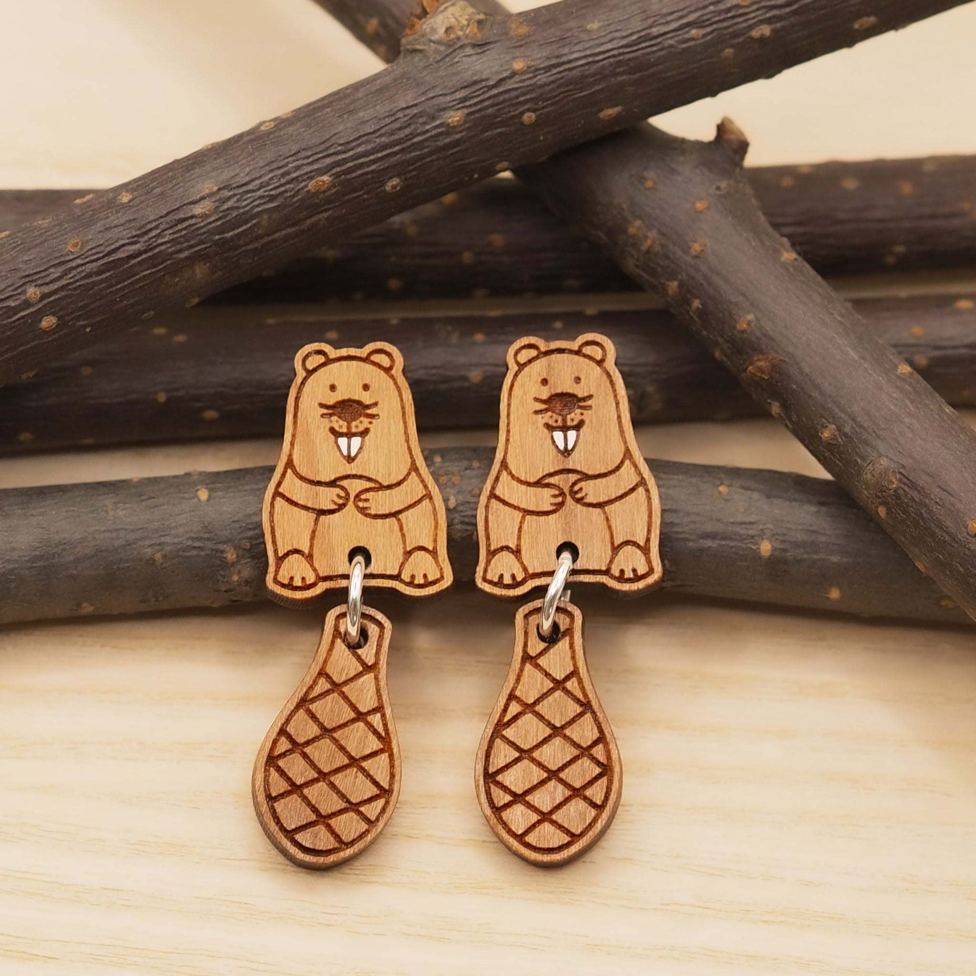 Cherry wood beaver stud earrings with dangling tails on surgical steel posts, eco-friendly gift box.