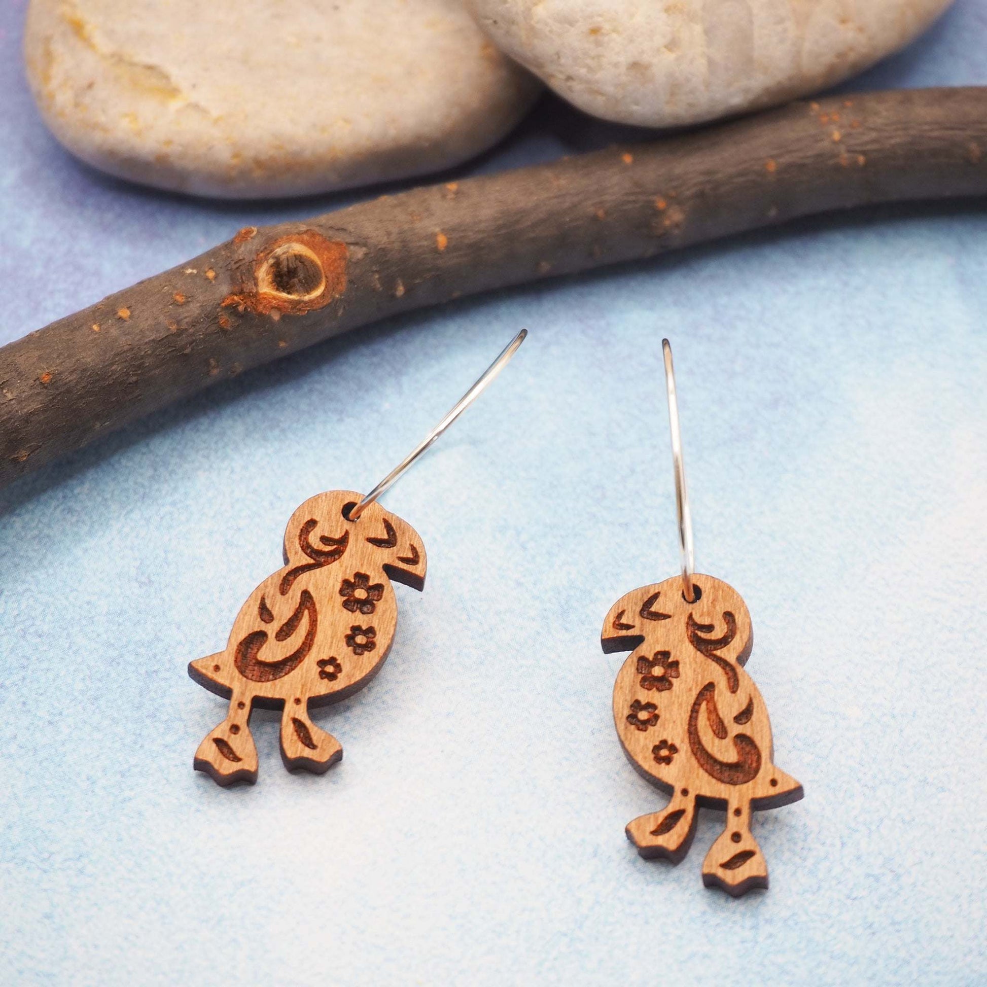 Wooden puffin engraved hoop earrings on sterling silver hoops with folk art pattern, displayed on blue background.