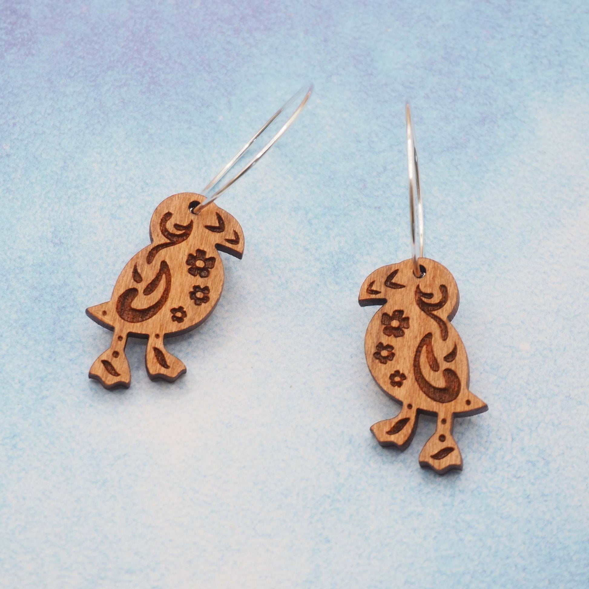 Wooden puffin engraved hoop earrings on sterling silver hoops against a blue background.