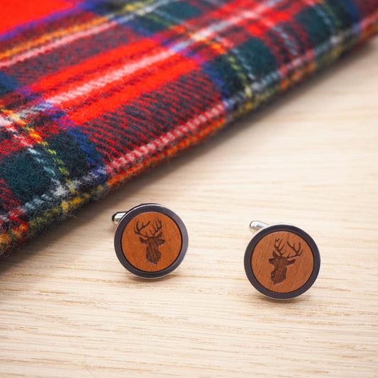 Stag head wooden cufflinks with engraved design on cherry wood, encased in silver tone rhodium, displayed on tartan cloth.