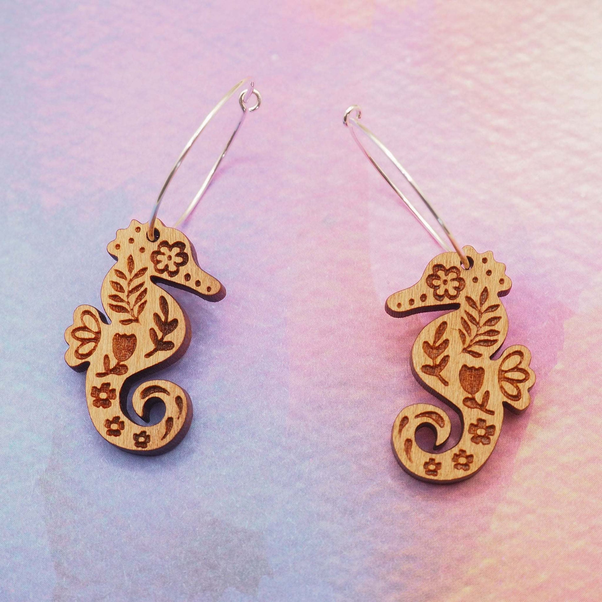 Seahorse engraved hoop earrings made from solid cherry wood with sterling silver hoops against a colorful background.
