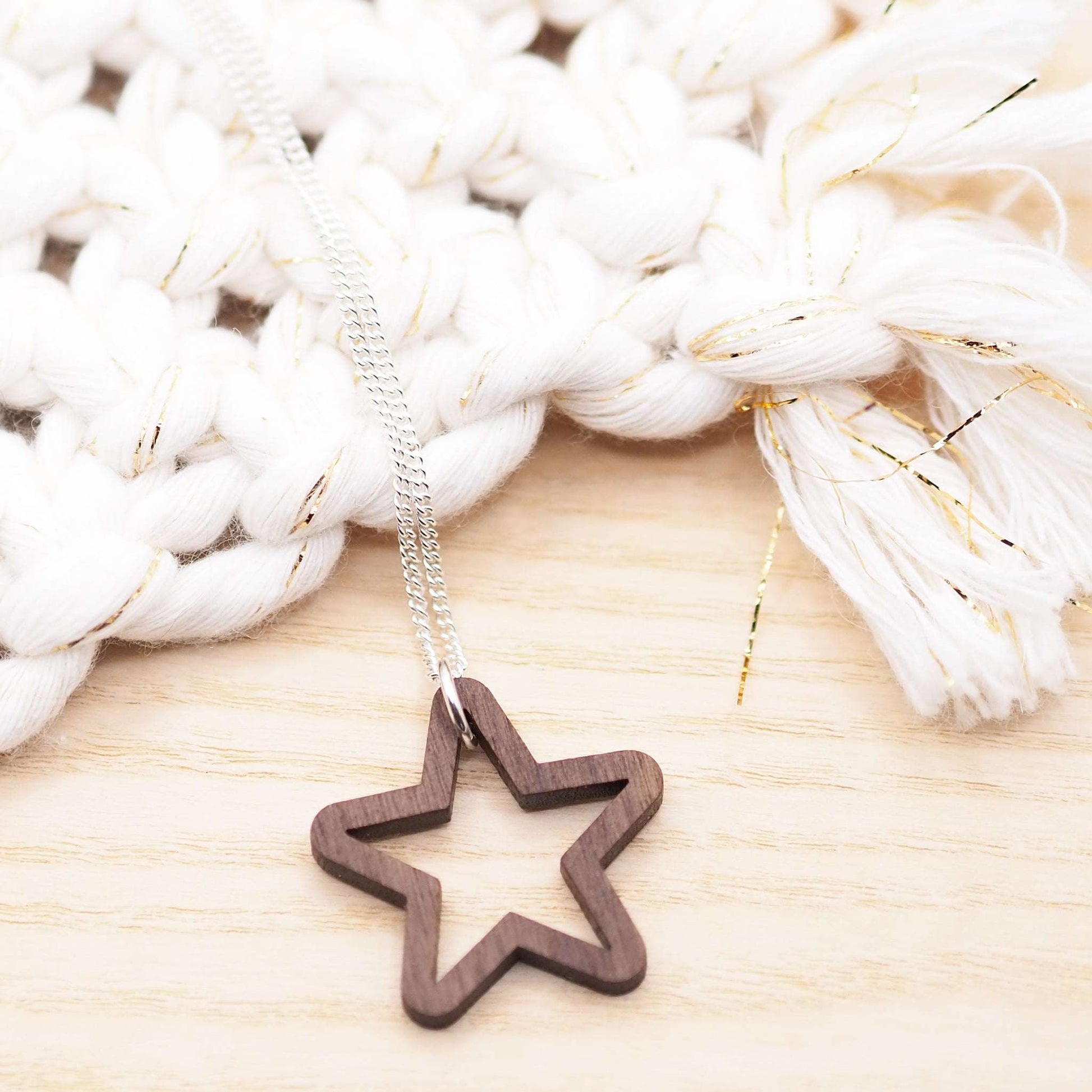 Chunky star necklace with wooden star pendant on silver chain against textured background.