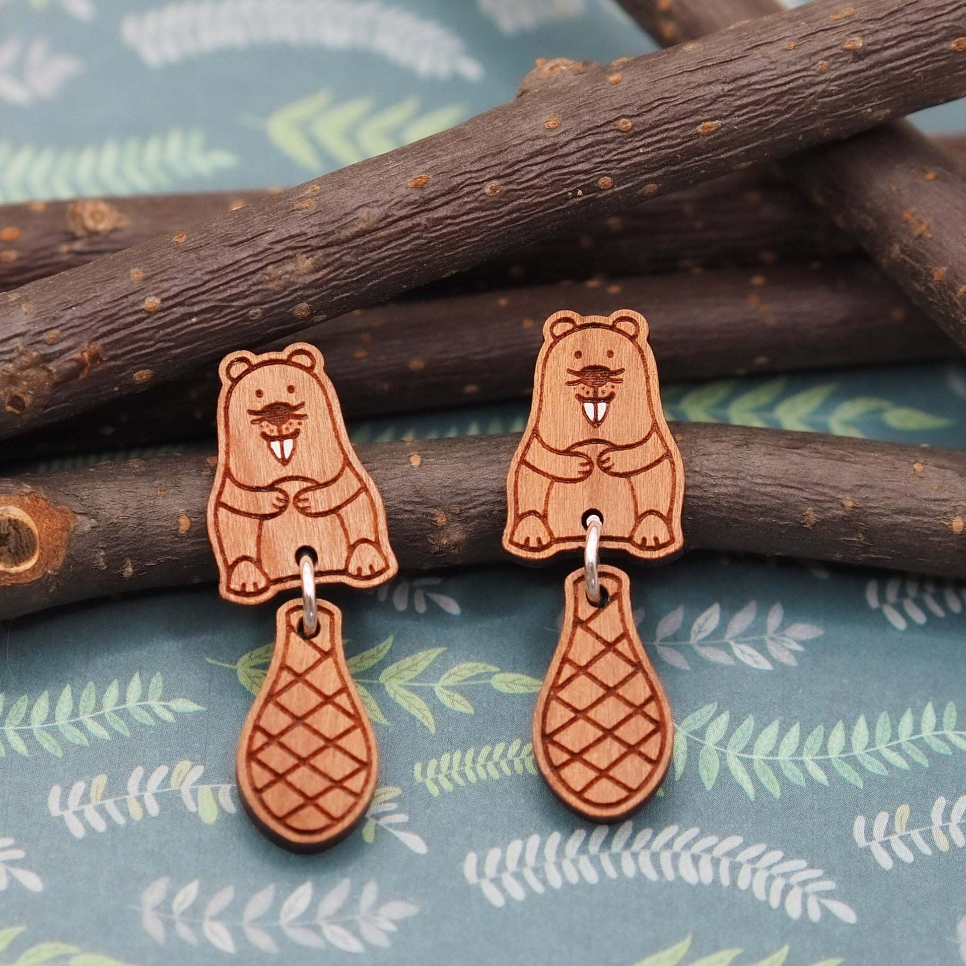 Cute beaver stud earrings made from cherry wood with dangling tails on eco-friendly gift box background.