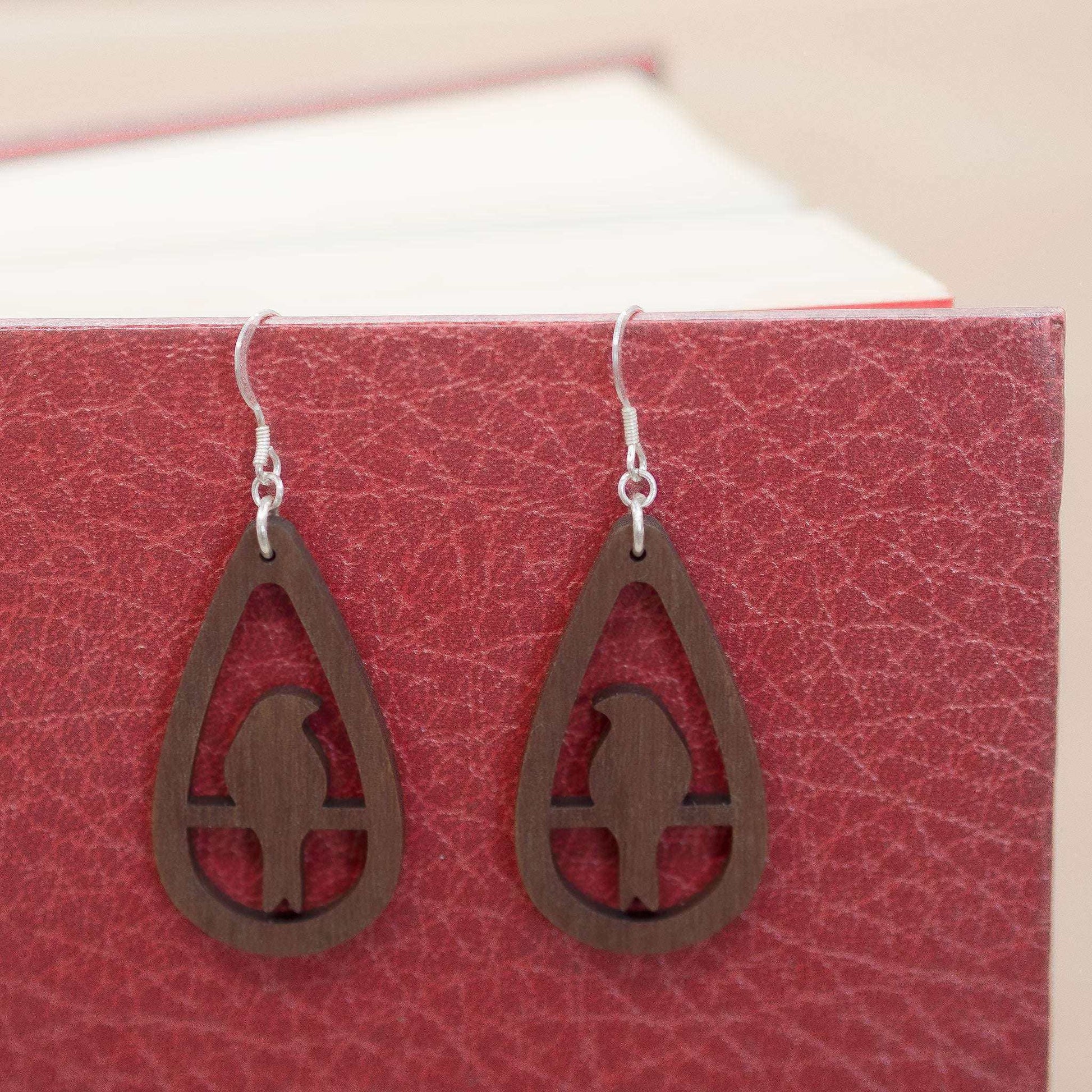 Teardrop bird drop earrings made from walnut wood with sterling silver hooks displayed on a book.