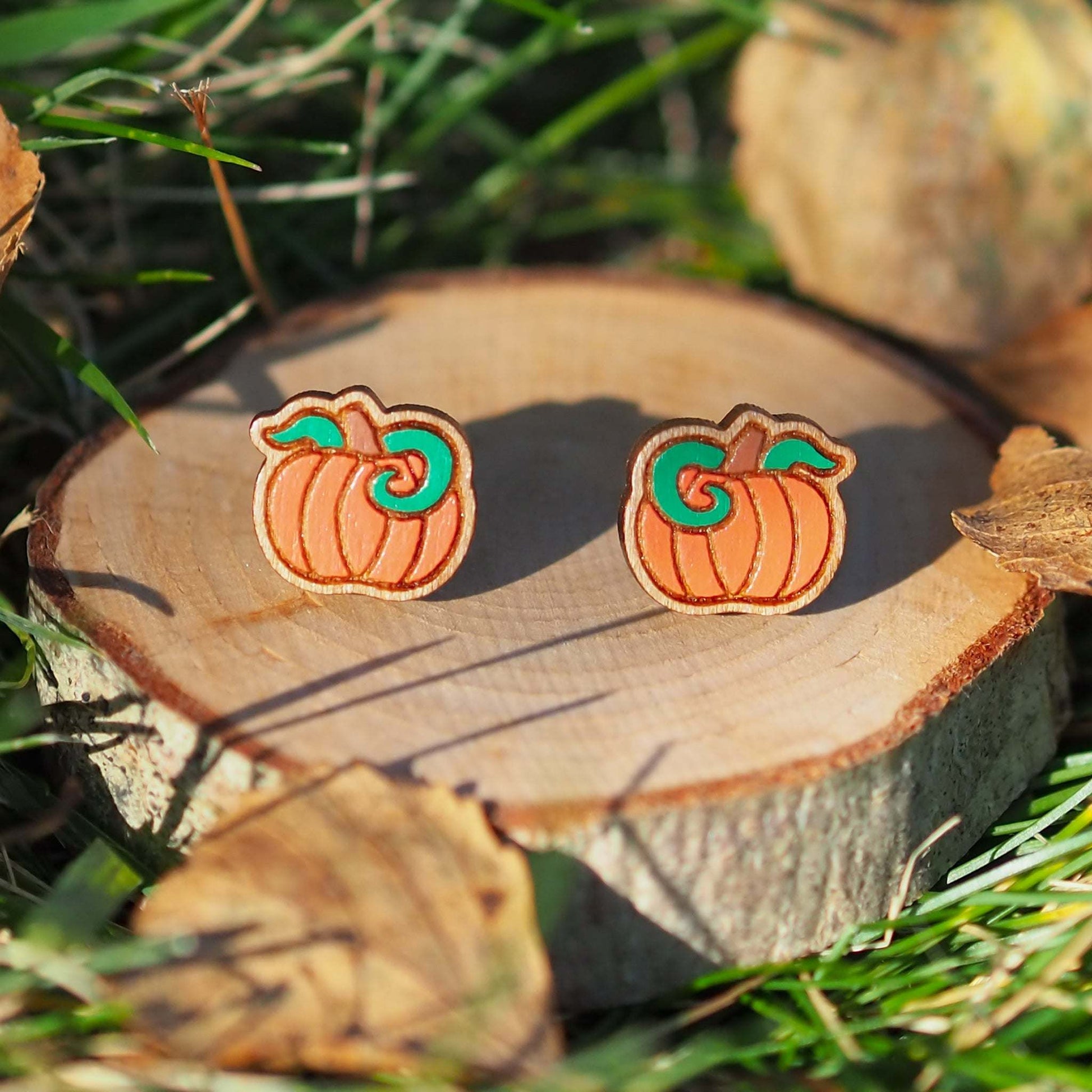 Cherry wood pumpkin stud earrings on grass, hand-painted, eco-friendly, perfect for Halloween.