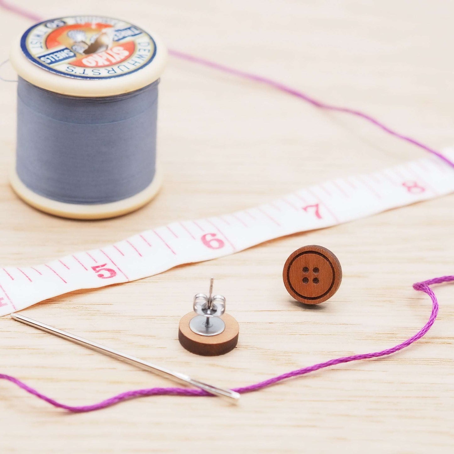 Cherry wood button stud earrings with surgical steel backs, displayed with sewing materials.