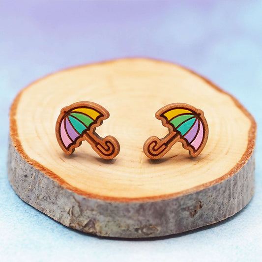Pastel rainbow umbrella wooden stud earrings on a wooden display.