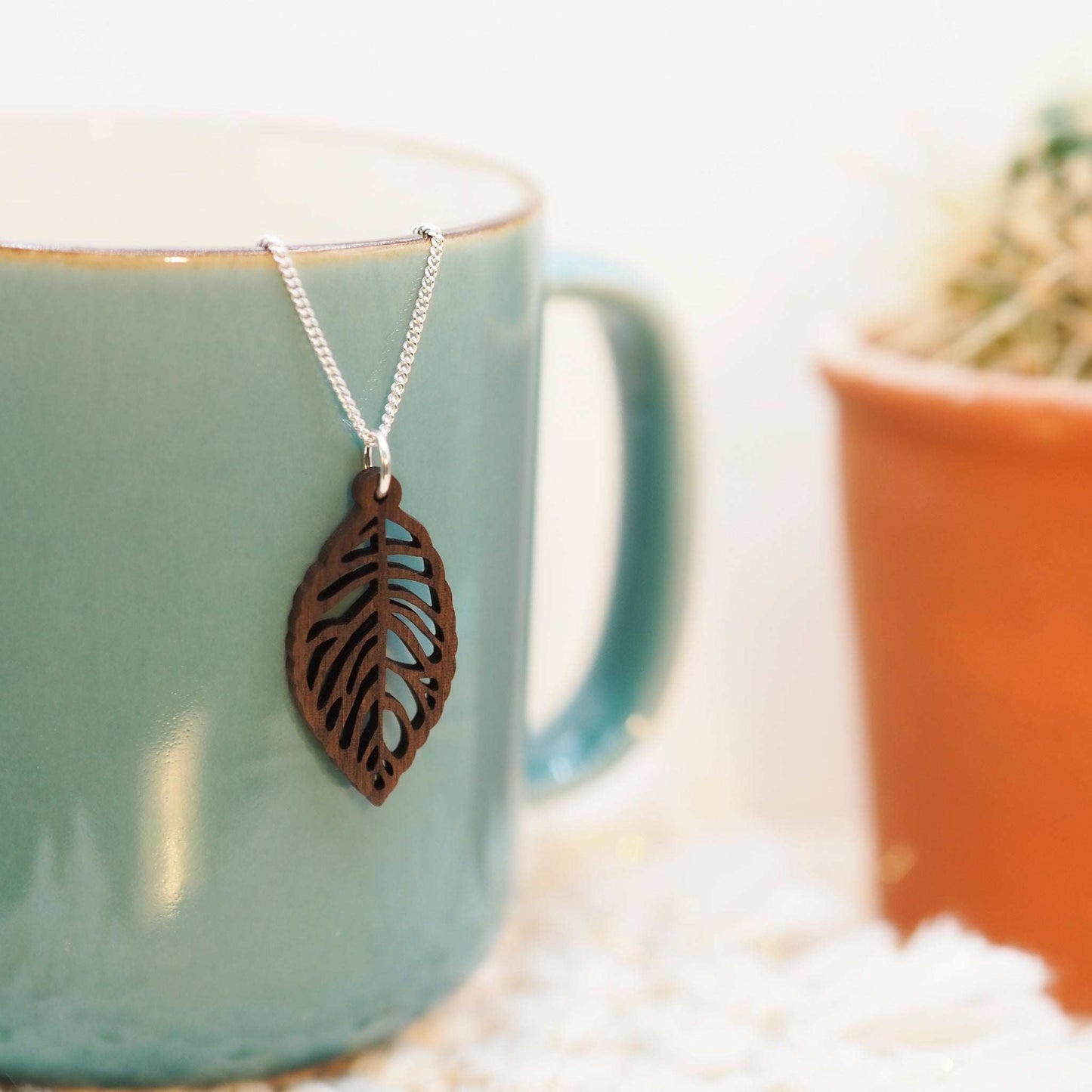 Leaf skeleton necklace made of walnut wood on a sterling silver chain, displayed on a mug.
