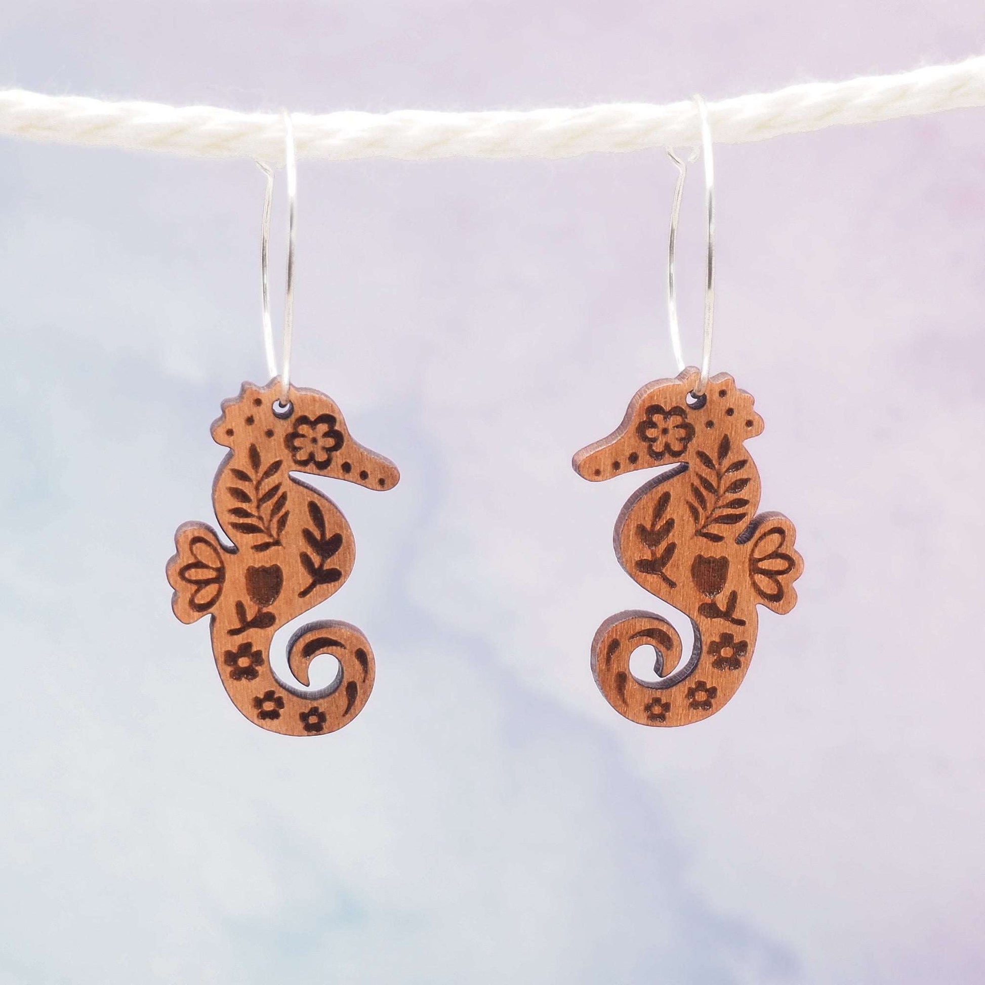 Seahorse engraved hoop earrings made from sustainable cherry wood with sterling silver hoops, featuring a folksy style pattern, and eco-friendly varnish.