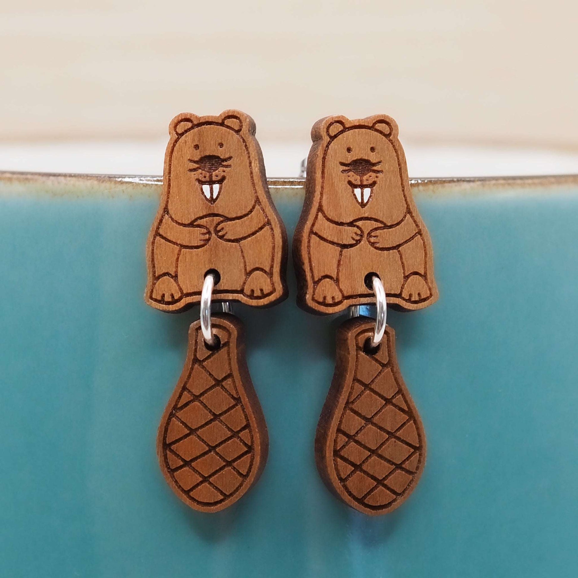 Cherry wood beaver stud earrings with dangling tails on surgical steel posts.