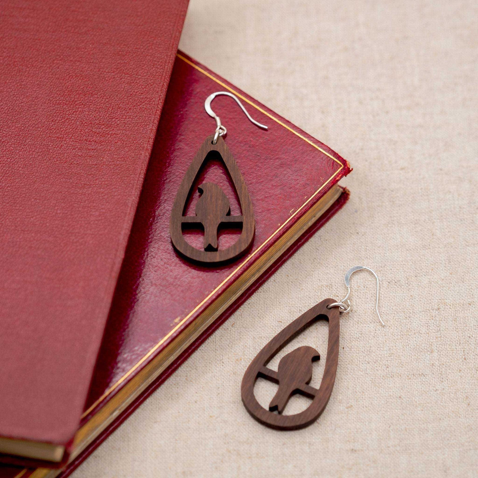 Teardrop bird drop earrings made from walnut wood with sterling silver hooks displayed on a red book.