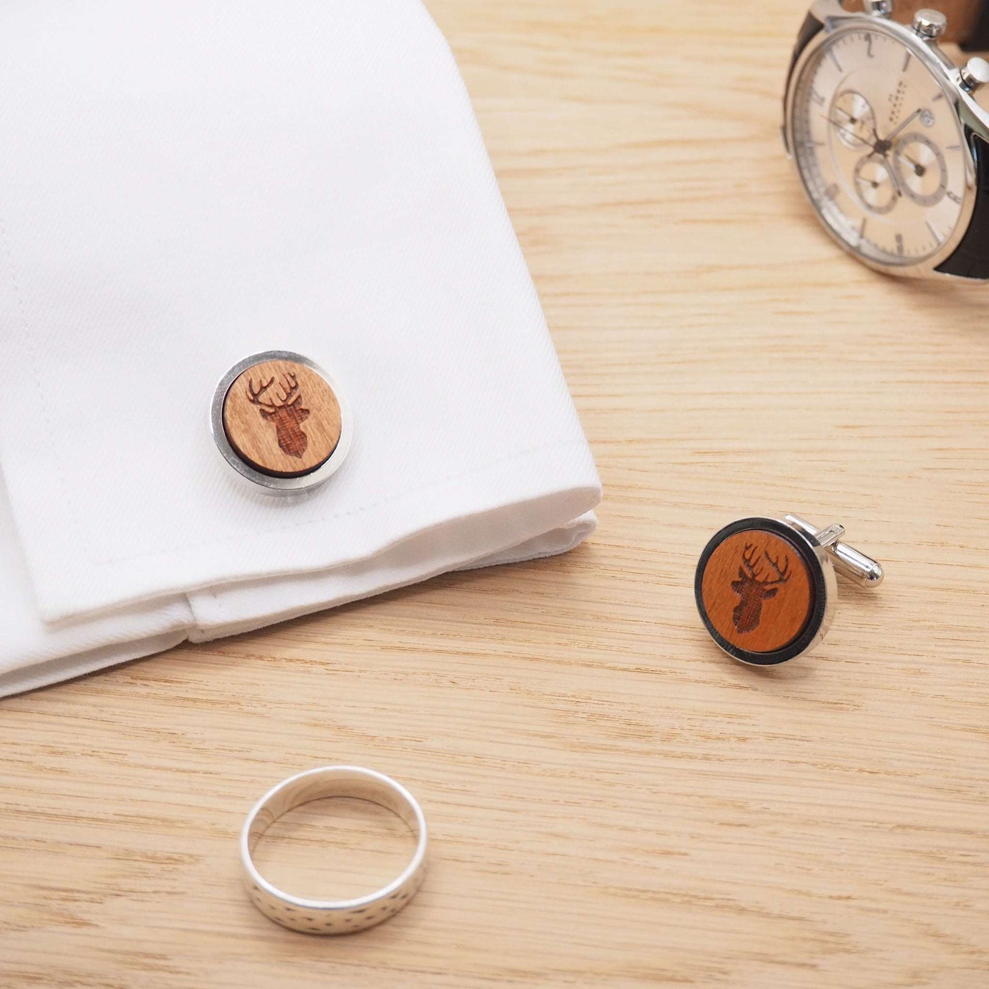 Stags head wooden cufflinks with engraved design on cherry wood in rhodium bezel, displayed on a white sleeve.