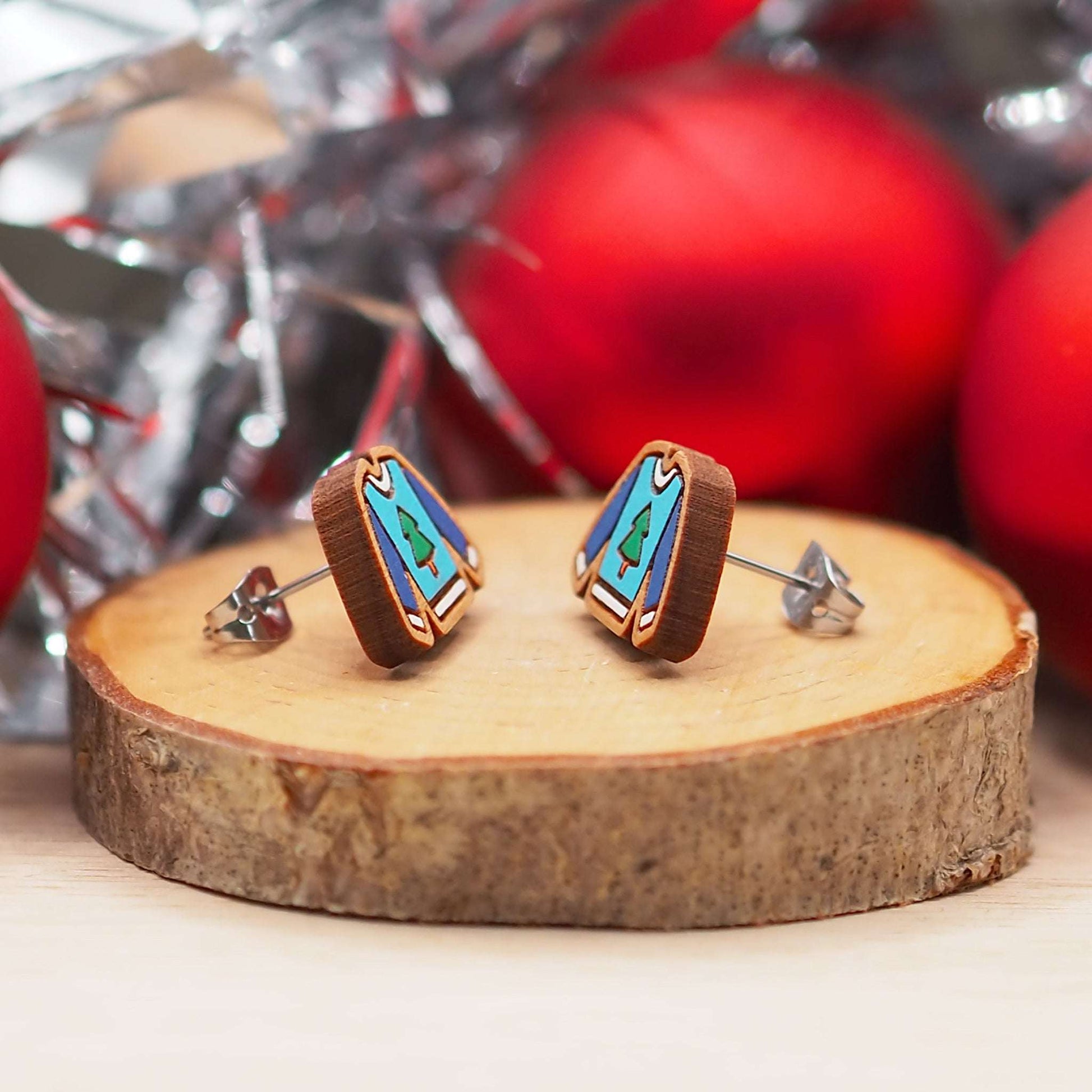 Christmas jumper stud earrings on cherry wood with festive design, mounted on surgical steel posts, displayed with holiday decor.
